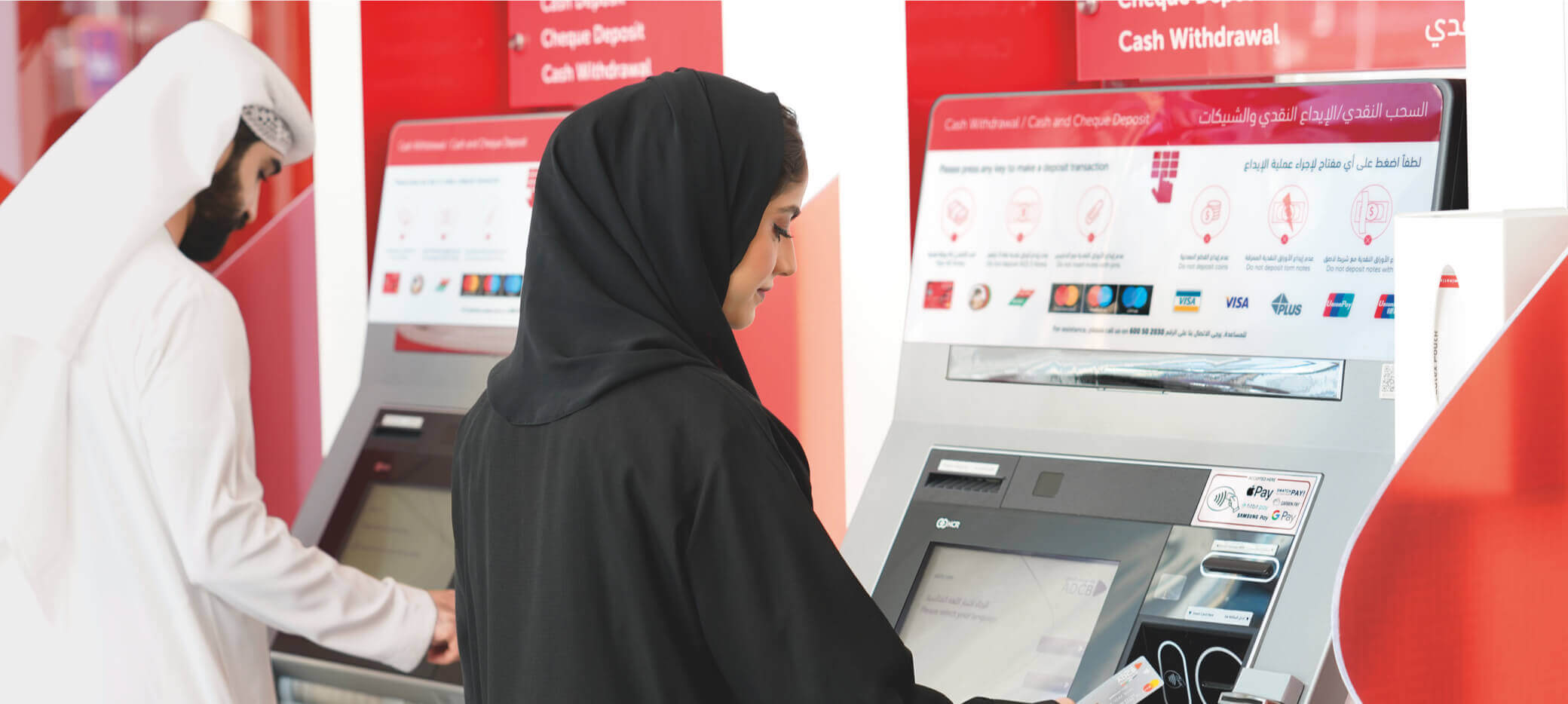 Two people using automated teller machines.